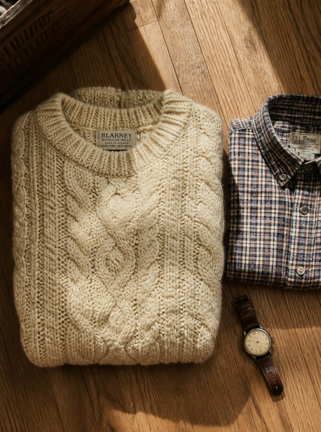 Cream cable knit jumper folded beside a checked shirt and watch